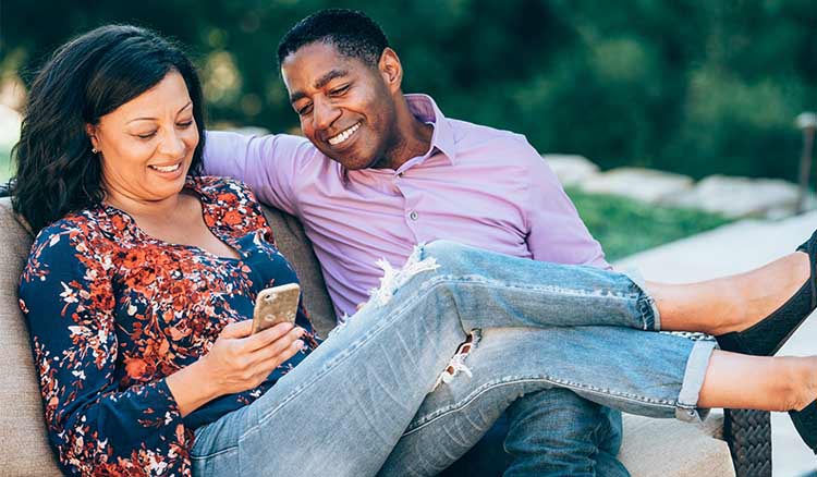 African American Couple On Bench Looking At Phone